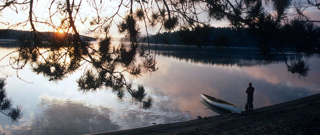 Man standing next to a canoe at sunset