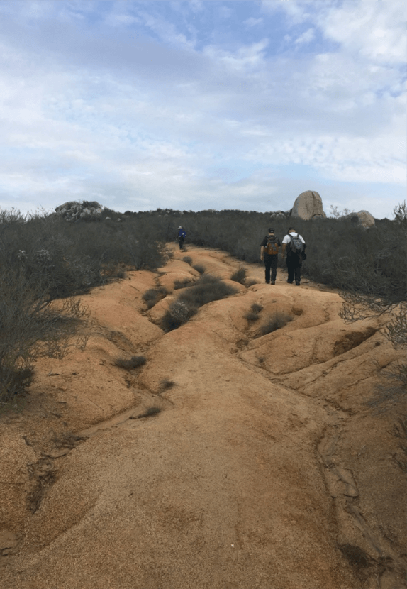 an old road that is no longer drivable with signs of runoff erosion with three people hiking